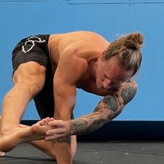 a man with tattoos on his arm and leg is doing a handstand in front of a blue wall