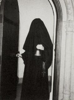 an old photo of a nun standing in front of a door with a bell on it