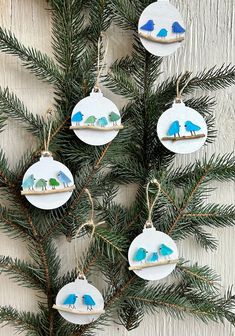 four ornaments hanging from a pine tree with blue birds on them and snow covered mountains in the background