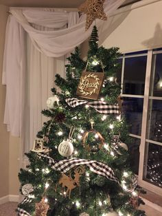 a decorated christmas tree in front of a window with white curtains and black and gold ornaments