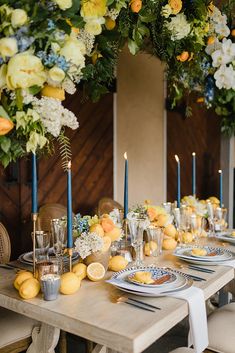 a table set with lemons, blue candles and white flowers on the tables for an elegant dinner