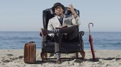 a man is sitting in a chair on the beach with an umbrella and suit case