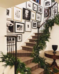 a staircase decorated with christmas greenery and framed pictures on the wall above it, along with potted plants