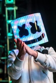 a man in a white jacket is holding his hands up to the camera while wearing a light - up mask