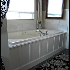 a bath tub sitting next to a window with curtains on the side and a rug in front of it