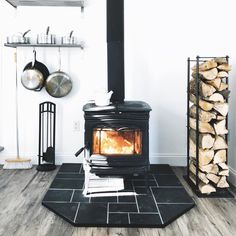 a wood burning stove sitting on top of a black rug next to a pile of logs