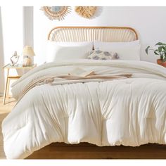 a bed with white comforter and pillows in a room next to a plant on the floor