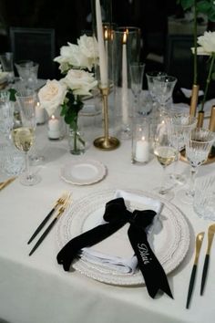 a white table with black napkins and silverware on it, surrounded by candles