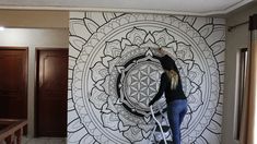 a woman standing on a ladder in front of a wall with a flower of life design