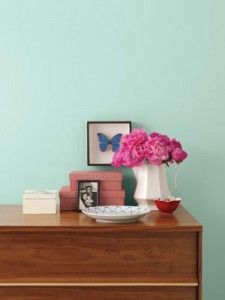 a wooden dresser topped with pink flowers and books next to a wall painted aqua blue