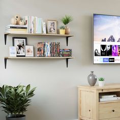 a television mounted to the side of a wall next to a wooden dresser and potted plant