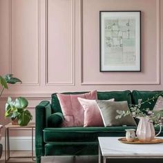 a living room with pink walls and green couches, coffee table and potted plants