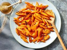 a white plate topped with cooked carrots next to a wooden spoon