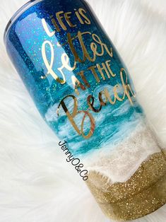 a blue and gold tumbler with the words life's better at the beach on it