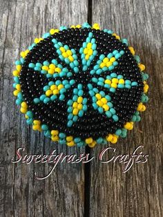 a black and yellow beaded brooch sitting on top of a wooden table