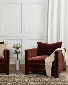 two red chairs sitting next to each other on top of a wooden floor in front of a white wall