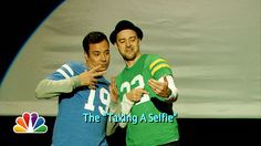 two men standing next to each other in front of a tv screen with the caption, the taking a selfie