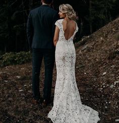 a bride and groom standing on a hill looking at each other with trees in the background