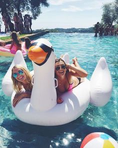 two girls are floating on an inflatable ducky at the pool with other people