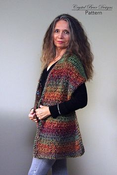 a woman standing in front of a white wall wearing a multicolored cardigan