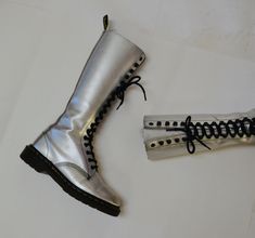 "Made in England by Dr. Martens Made in England by Dr. Martens Silver metallic leather Print Combat boots Size -VTG Size 4 UK US Womens aprx 6 Leather upper Rubber souls 10 3/8\" length outer sole 9 1/8\" length inner sole 4\" width outer sole 3 3/4\" width inner sole Shaft Height 12 1/2\" from heel Used Vintage condition with below points * wear/scuffs on outside of shoe where the silver has worn * Some wear on the inside of the insoles * Some wear on the soles * Lots of life in them! Price is Shiny Doc Martens, Silver Doc Martens, Gothic Silver Boots With Metal Feet, Grunge High-top Moto Boots With Metal Feet, Silver Platform Punk Boots, Dr Martens Boots Women, Lace Up Knee High Boots, Silver Leather Knee-high Boots, Silver Boots