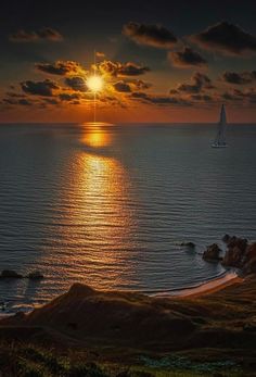 the sun is setting over the ocean with a sailboat in the water below it