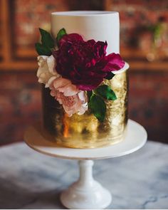 a white and gold wedding cake with red flowers on the top is featured in an instagram post