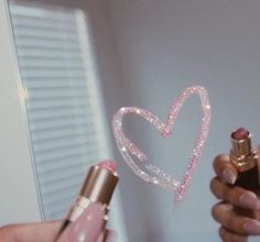 a woman holding a lipstick in her hand with a heart drawn on the bottle next to it