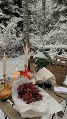 a table topped with lots of food and candles in front of snow covered forest trees