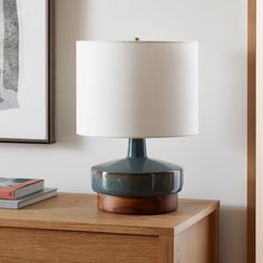 a lamp sitting on top of a wooden dresser next to a painting and a book