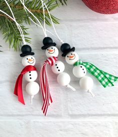 three snowman ornaments hanging from a christmas tree