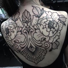 the back of a woman's shoulder with black and white floral tattoos on it