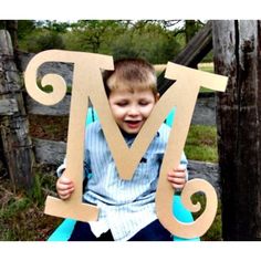 a young boy sitting on top of a wooden letter