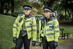 two police officers standing next to each other in front of a park bench and trees