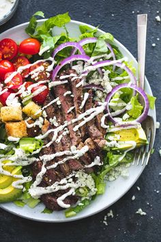 a steak salad with dressing on a white plate