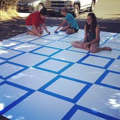 three children are sitting on the ground with blue squares painted on it and one child is drawing