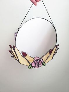 a hand holding a stained glass mirror with a flower on the front and side hanging from it