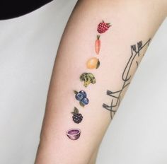 a woman's arm with fruits and vegetables painted on her left arm, including raspberries, oranges, blueberries, lemons, strawberries