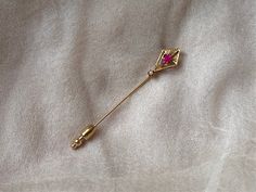 "This enchanting stick pin features a glittering, faceted lab-made ruby stone set in a delicately etched 10k gold arts-and-crafts style setting with a seed pearl at the bottom. It is marked on the pin portion as being 10k gold along with a partial  maker's mark that is hard to read.  It weighs 1.05 g (without fob), measures 2.5\" x 3/8\" and is in great antique condition." Art Deco Ruby Jewelry Gift, Art Deco Ruby Jewelry As A Gift, Elegant Handmade Lapel Pin As Gift, Elegant Handmade Lapel Pin For Gift, Art Deco Gold Brooches As Gift, Gold Art Deco Brooches As A Gift, Handmade Elegant Gold Lapel Pin, Elegant Handmade Gold Lapel Pin, Elegant Yellow Gold Lapel Pin For Gifts