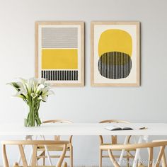 two paintings on the wall above a table with four chairs and a vase filled with flowers