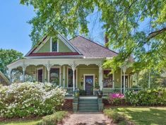 a green house with white trim and flowers in the front yard on a sunny day