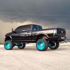 a black truck with turquoise rims parked in front of a dark cloud filled sky