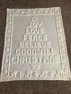 a white crocheted christmas tree on the floor with words written in it and an ornament