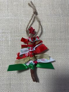 a christmas tree ornament hanging from a string on a white fabric background with red, green and gold ribbons