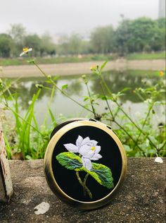 an embroidered white flower sitting on top of a wooden table next to a body of water