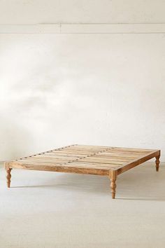 a wooden bed frame sitting on top of a white floor next to an empty wall