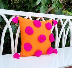 an orange pillow with pink pom - poms on it sitting on a white bench