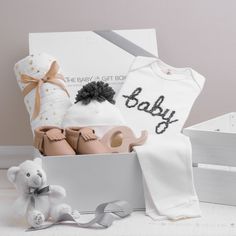 a baby gift box with clothing, shoes and a teddy bear sitting next to it