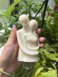 a hand holding a small white sculpture in front of a potted plant with green leaves