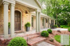 a brick house with two porches and steps leading up to the front door, surrounded by greenery